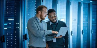 Two data storage pros work on a laptop among servers in a data center.